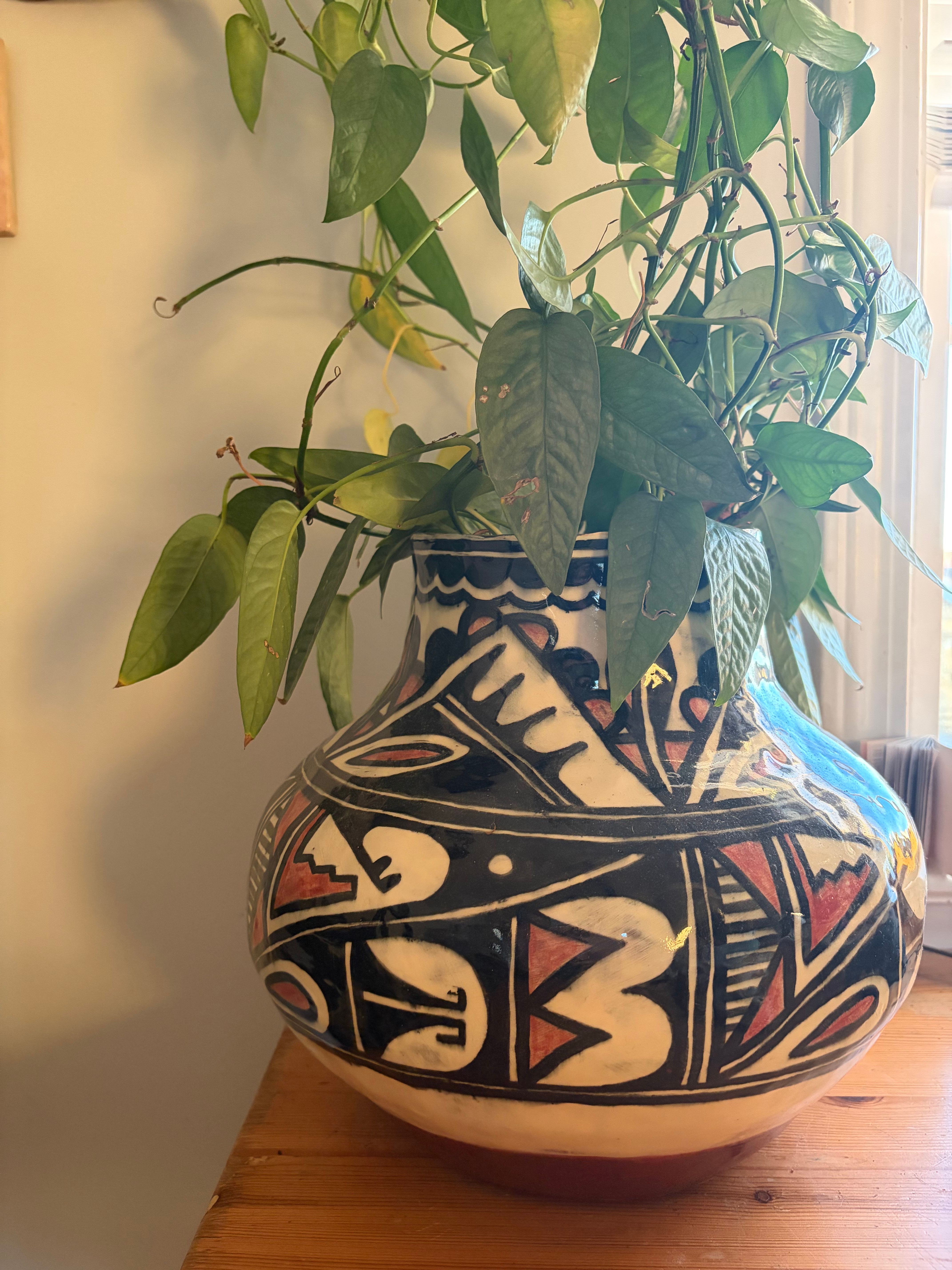 Christina's first coil-built vase: a round stoneware pot painted in black, cream and terracotta geometric patterns, holding a trailing plant
